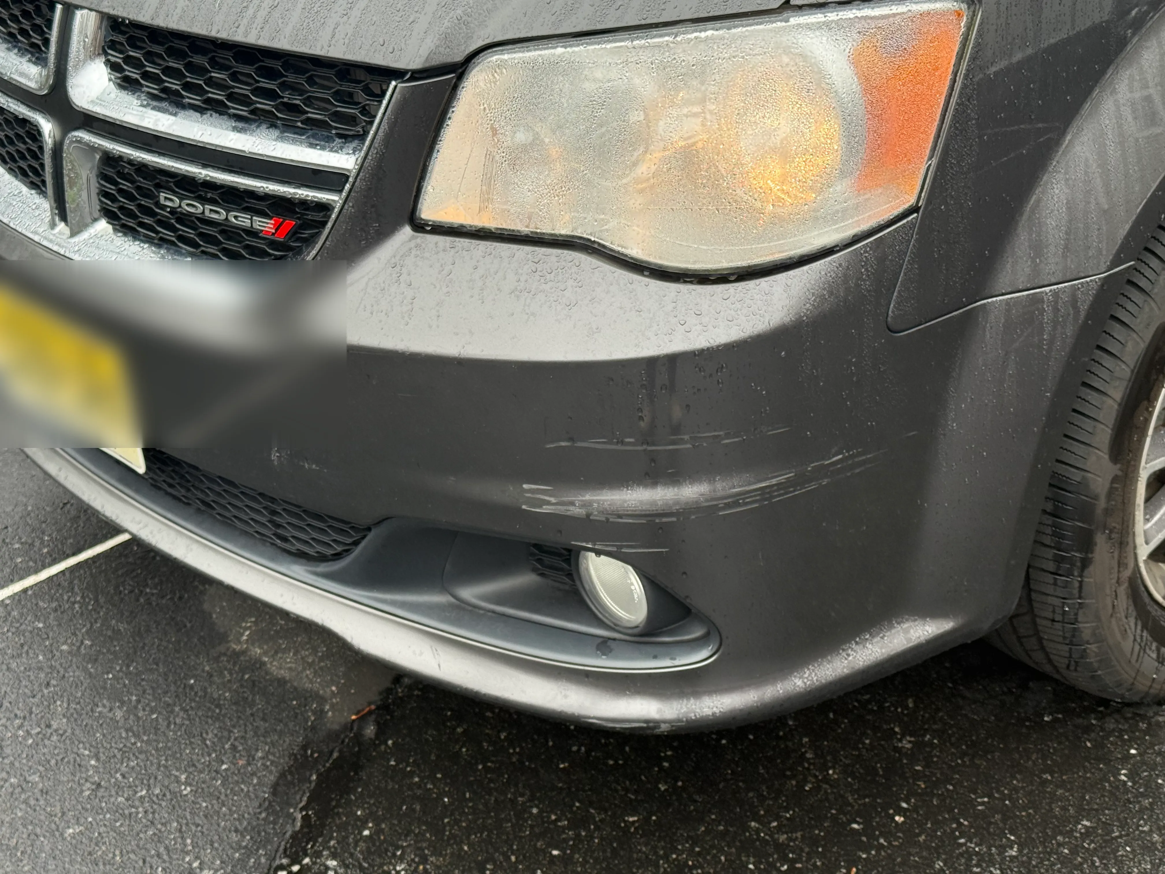 Gray Dodge Grand Caravan front bumper with visible scratches across the lower section, before repair.